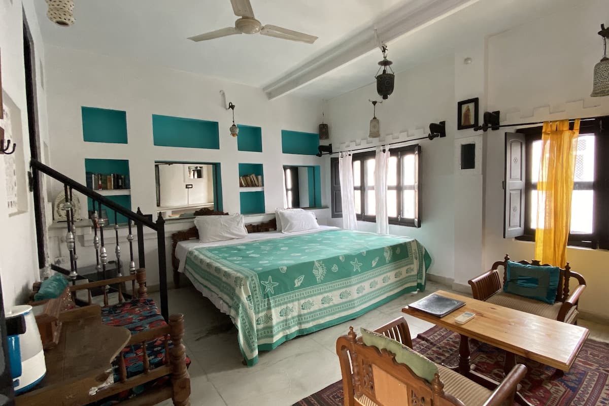 A bedroom with a bed, a desk, a chair, a window with curtains, a ceiling fan, and a staircase.