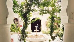 Une entrée en arc de cercle agrémentée d’une fontaine et de plantes en pot.