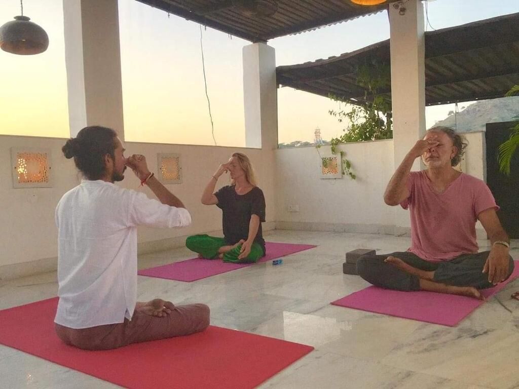 A group of people sitting on yoga mats in a room with a tiled floor and a high ceiling.