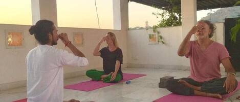 A group of people sitting on yoga mats in a room with a tiled floor and a high ceiling.