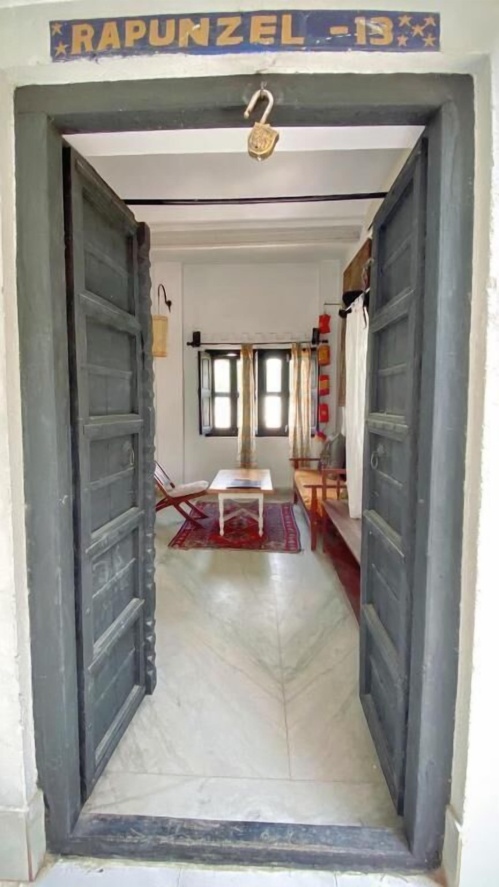 A hallway with two large wooden doors, a small table with a chair, and a window with curtains.