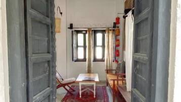 A hallway with two large wooden doors, a small table with a chair, and a window with curtains.