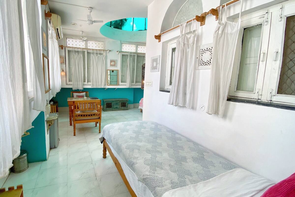 A bedroom with a bed, a wooden chair, a small table, and a window with curtains.