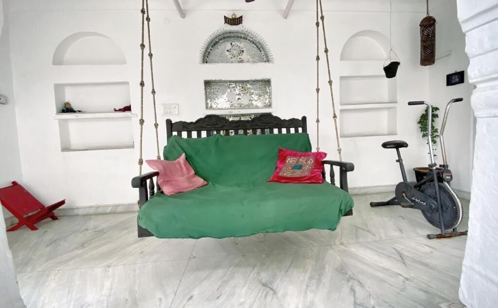 Una habitación con un sofá verde, cojines rojos y rosados, una bicicleta estática colgante y una silla roja.