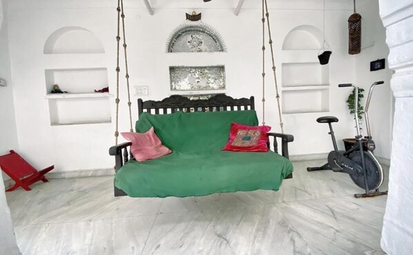 Una habitación con un sofá verde, cojines rojos y rosados, una bicicleta estática colgante y una silla roja.