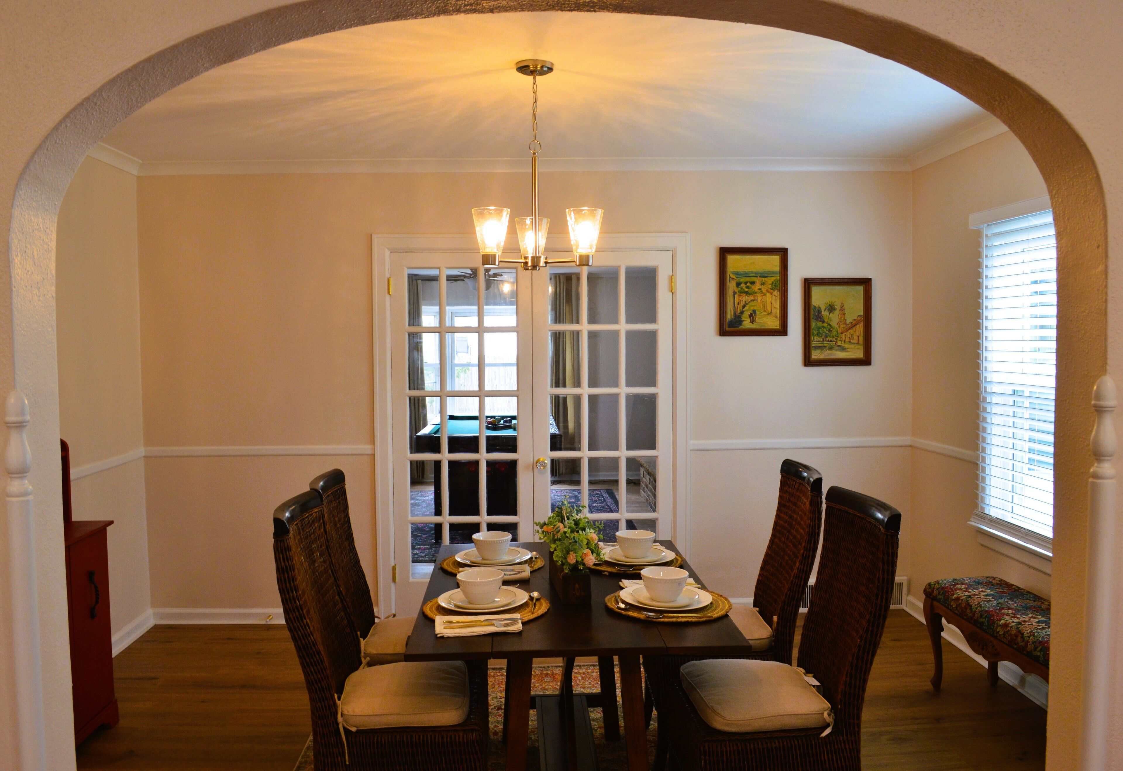 A dining area with a dark wooden table set for four, surrounded by wicker chairs with cushions.
