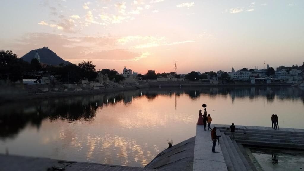A calm river with people walking along the embankment during sunset.