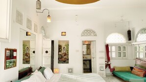 A spacious bedroom with a large bed, a small seating area, and a decorative ceiling light. - Dia homestay (Pushkar)