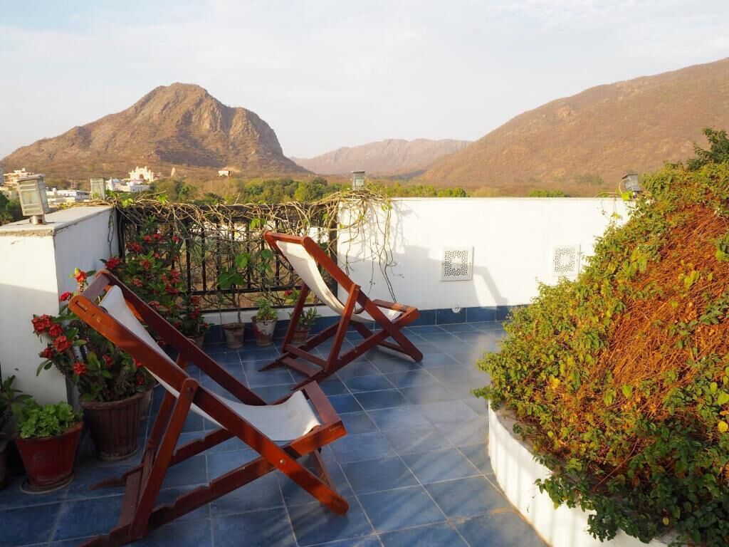 A rooftop terrace with two wooden chairs, potted plants, and a view of mountains.