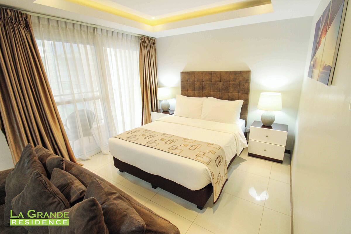 A hotel room with a large bed, two bedside tables, a nightstand, and a couch.