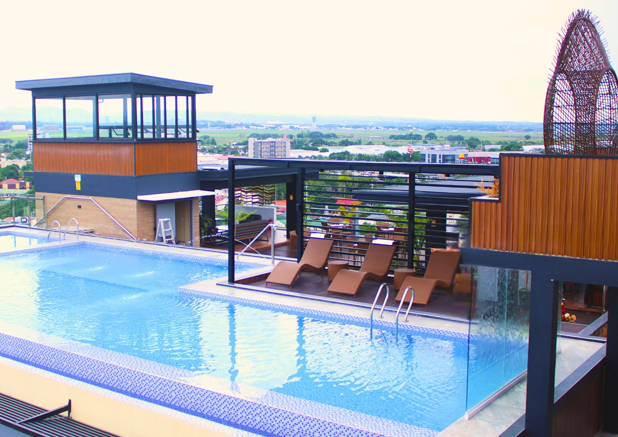 Una piscina en la azotea con sillones de descanso, una torre de control y vistas de la ciudad.