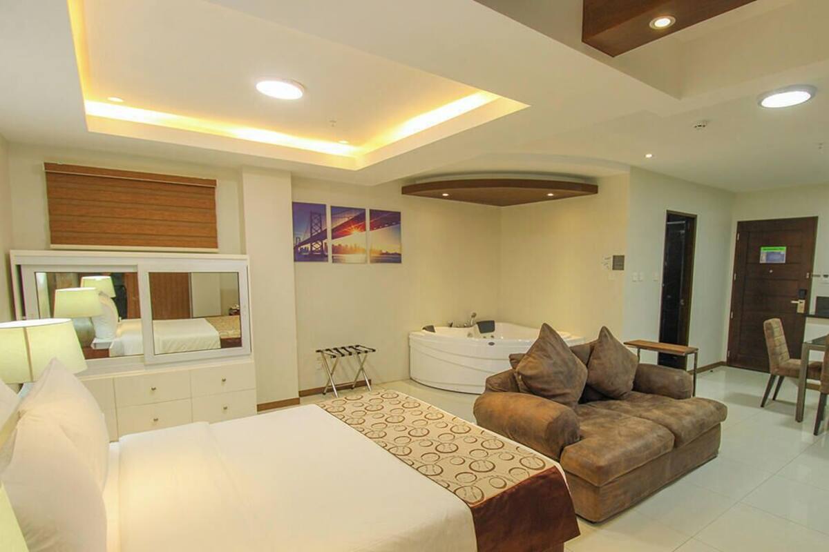 A modern hotel room with a bed, a sofa, a desk, and a bathroom.