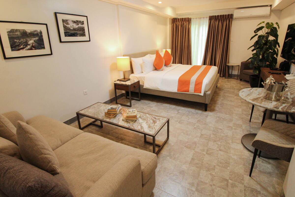 A hotel room with a bed, a sofa, a coffee table, a desk, and a dining table.