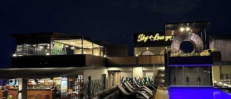 A nighttime view of a hotel with a pool, a bar, and a sign reading "Sky Lounge".