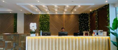 A modern reception desk with a wooden finish, a vertical garden, and a geometric patterned wall.