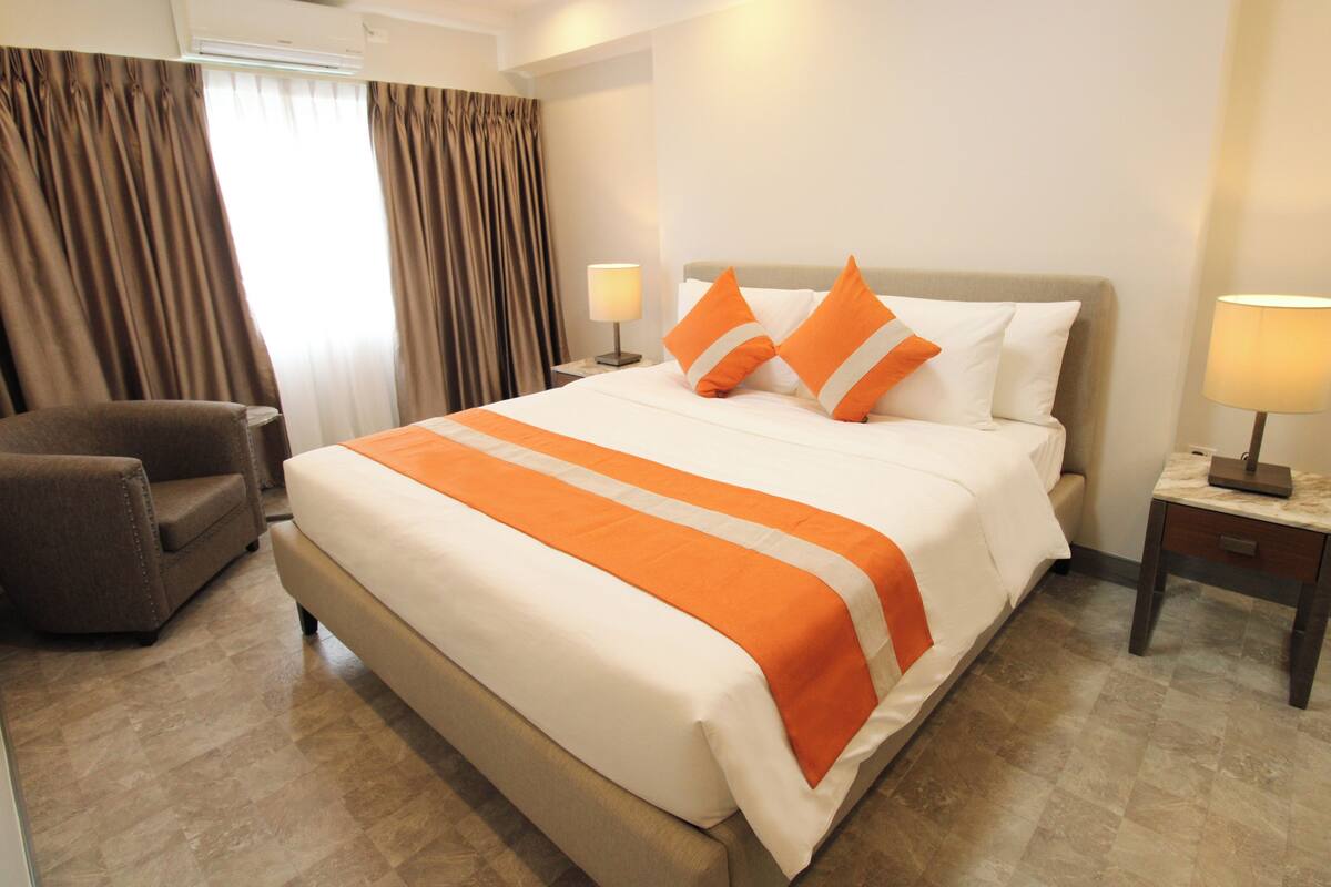 A hotel room with a large bed, two bedside tables, a chair, and a window with curtains.