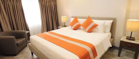 Una habitación de hotel con una cama grande, dos mesitas de noche, una silla y una ventana con cortinas.