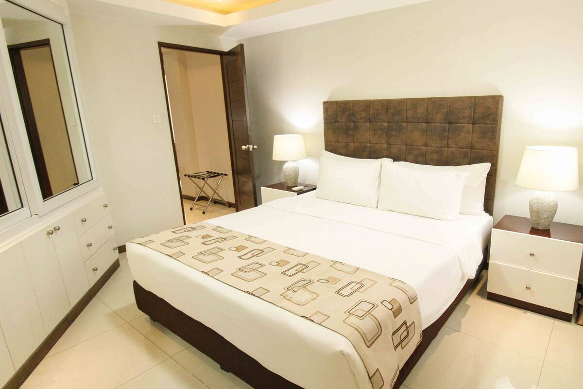 A hotel room with a large bed, two bedside tables with lamps, a wardrobe, and a mirror.