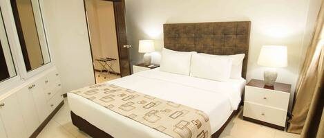 Habitación de hotel con una cama grande, dos mesitas de noche con lámparas, un armario y un espejo.