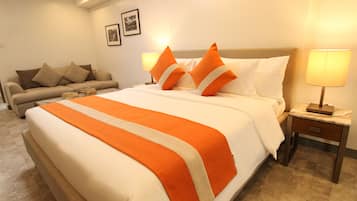 A hotel room with a large bed, a sofa, and a nightstand with a lamp.