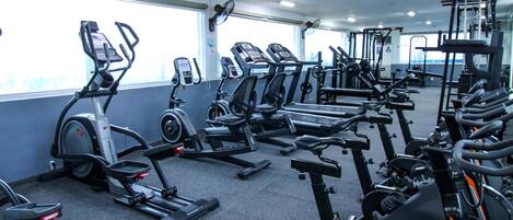 A gym with various exercise machines, large windows, and a ceiling fan.