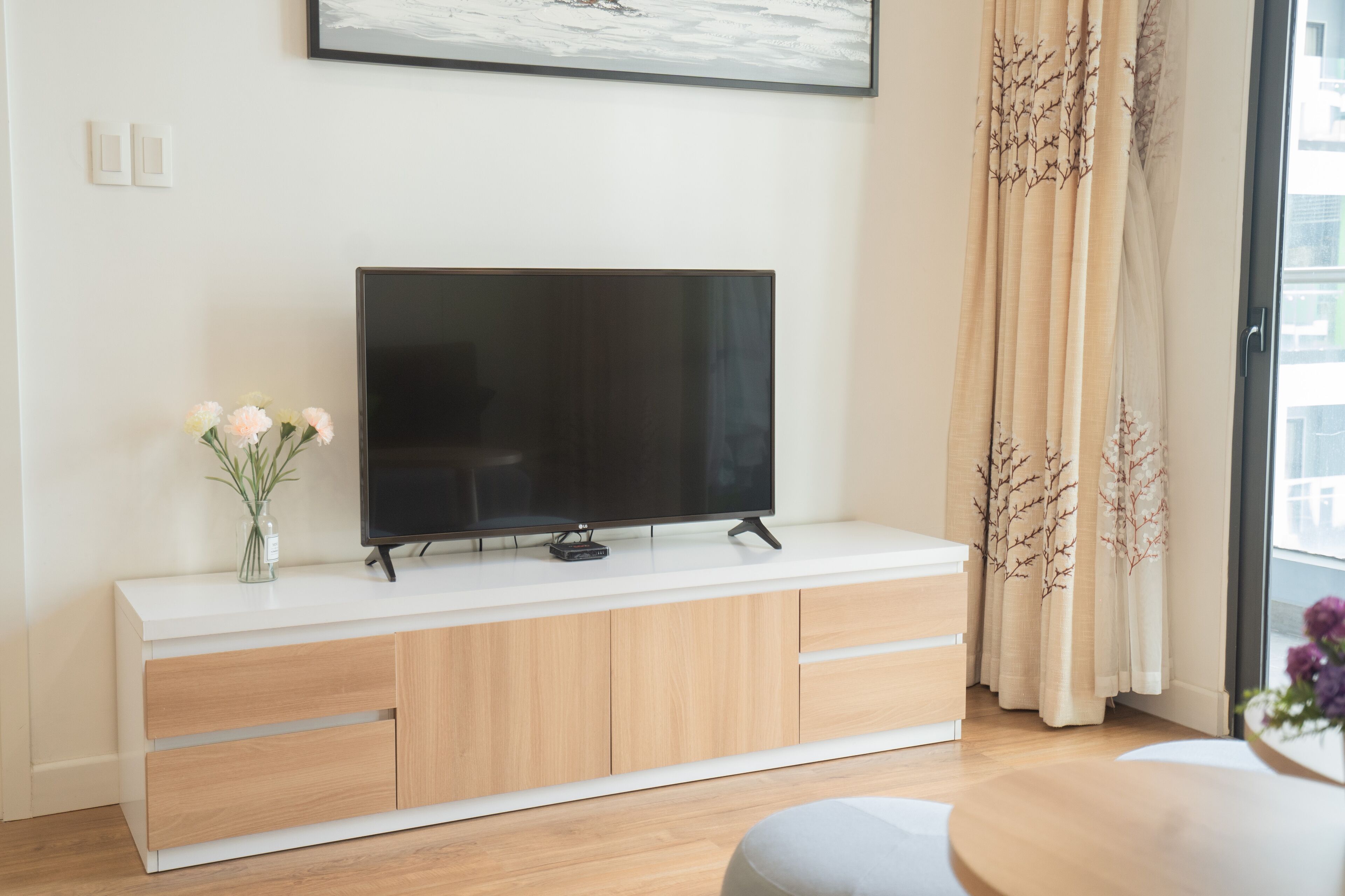 Ein modernes Wohnzimmer mit einem Flachbildfernseher auf einer weißen Konsole, Holzkredänzen und einer Vase mit Blumen.