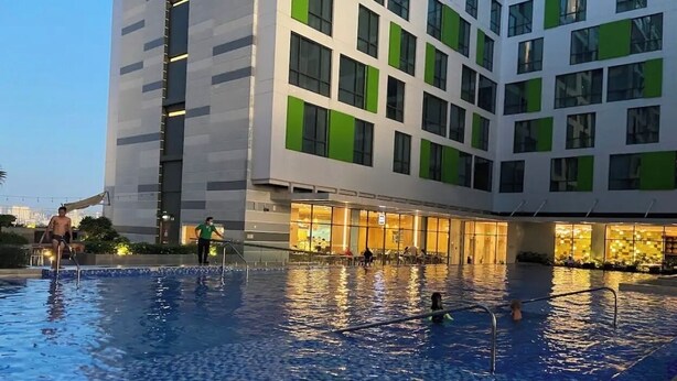 Una piscina con suelo de baldosas y un edificio con varias ventanas al fondo.