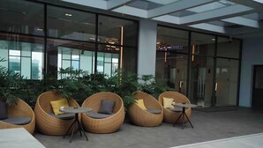 Un área de estar interior moderna con sillas y mesas de mimbre, ventanas amplias y plantas de interior.