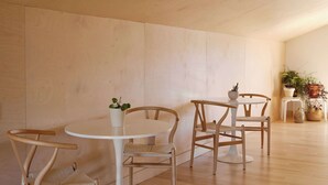 Een kamer met houten vloer, een ronde tafel, twee stoelen en een potplant.