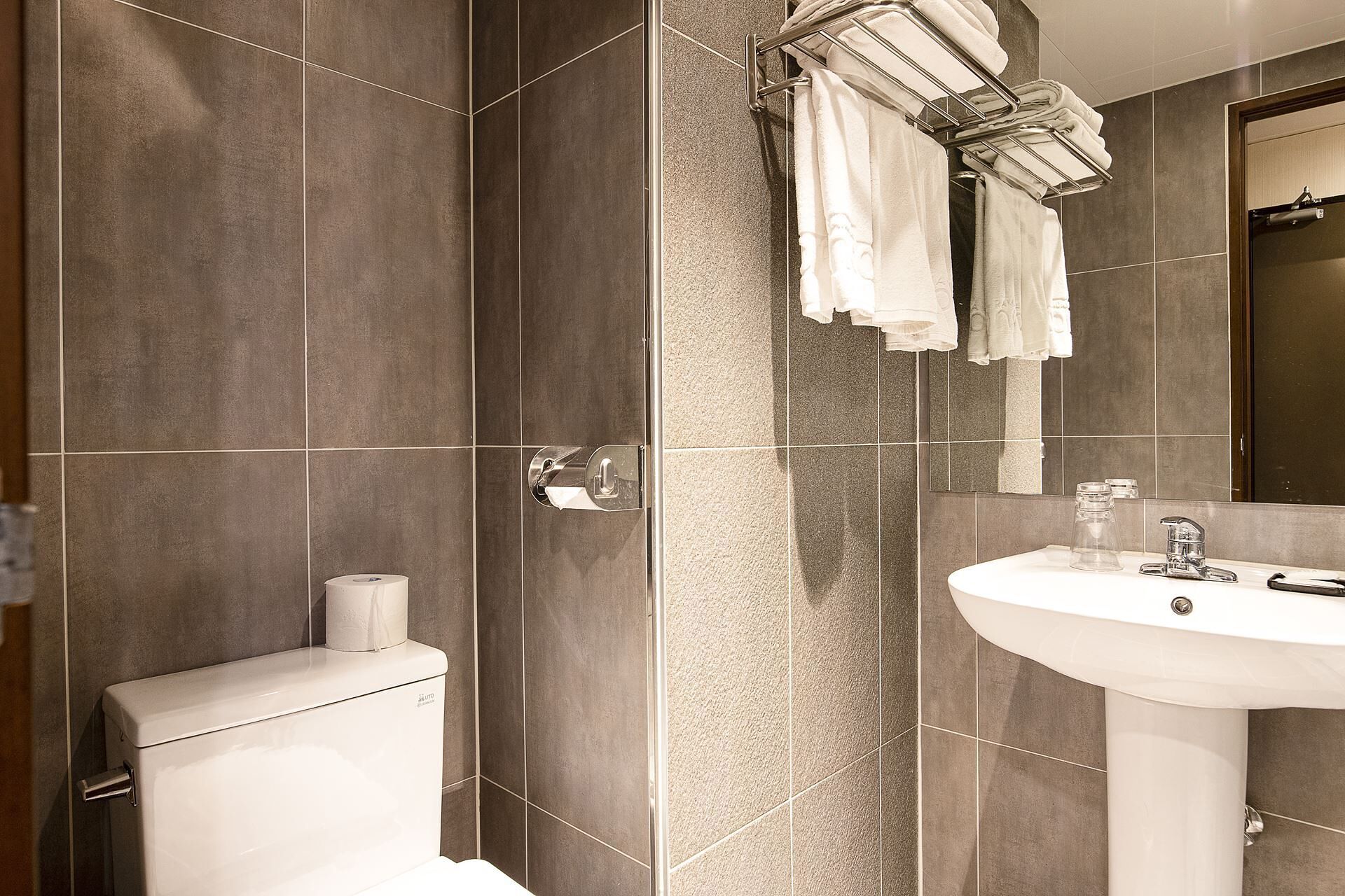A bathroom with a toilet, a towel rack with towels, a sink, and a mirror.