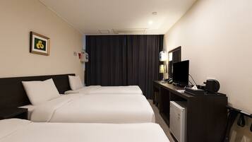 A hotel room with two beds, a desk with a computer, a coffee maker, and a small refrigerator.