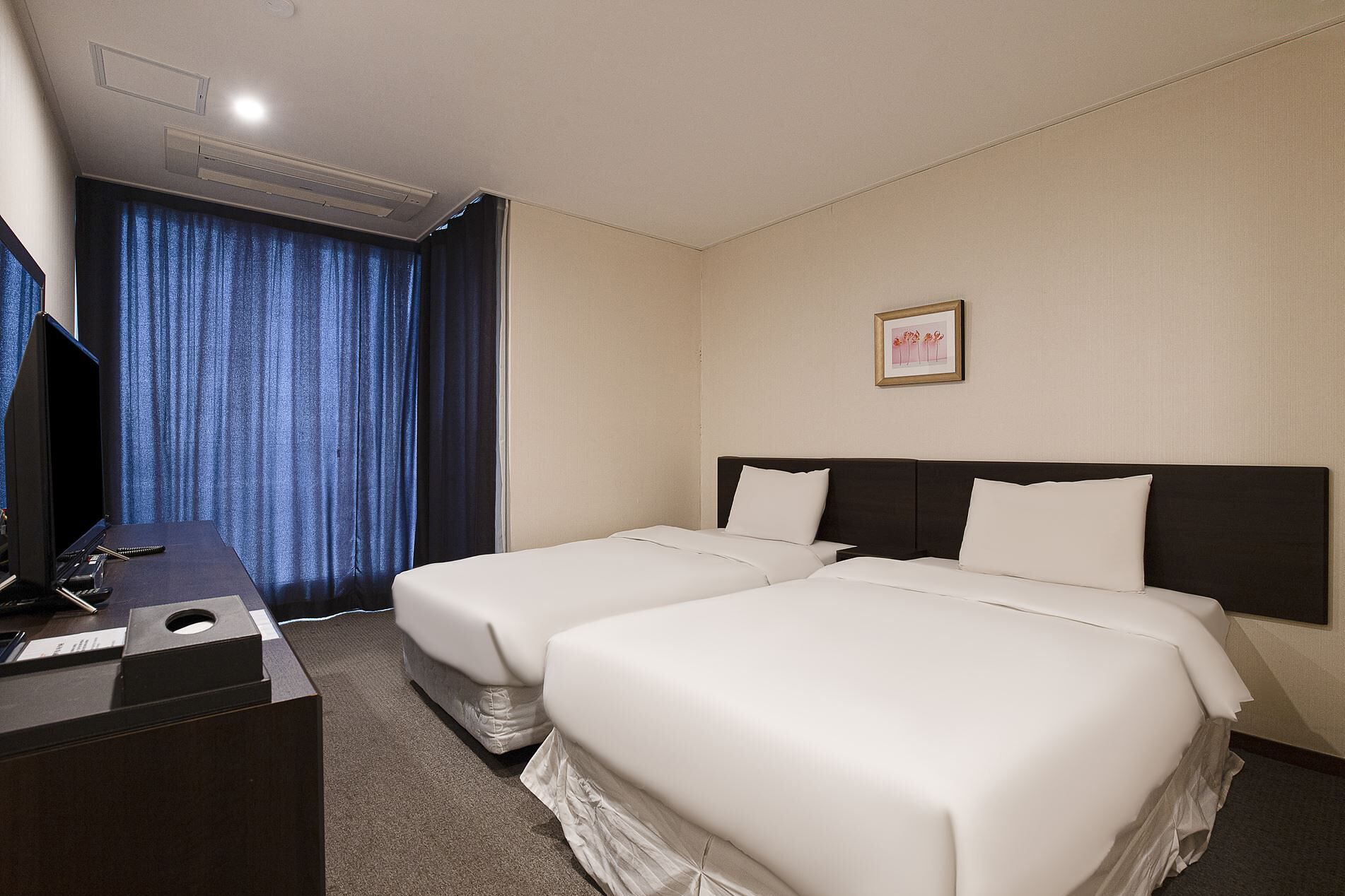 Habitación de hotel con dos camas, un escritorio, televisor y ventana con cortinas.