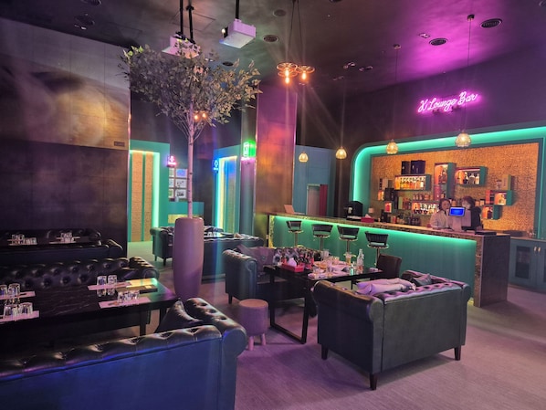 Un espace bar agrémenté d'un néon, de sièges en cuir et d'un comptoir où travaille un barman.