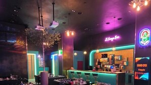 Uma área de bar com um letreiro de neon, balcão e assentos.