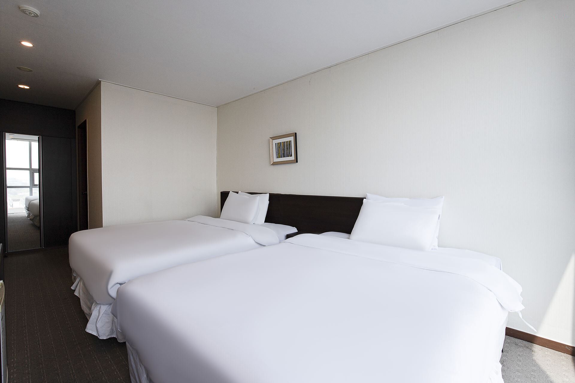 A hotel room with two beds, a large window, and a door leading to a balcony.