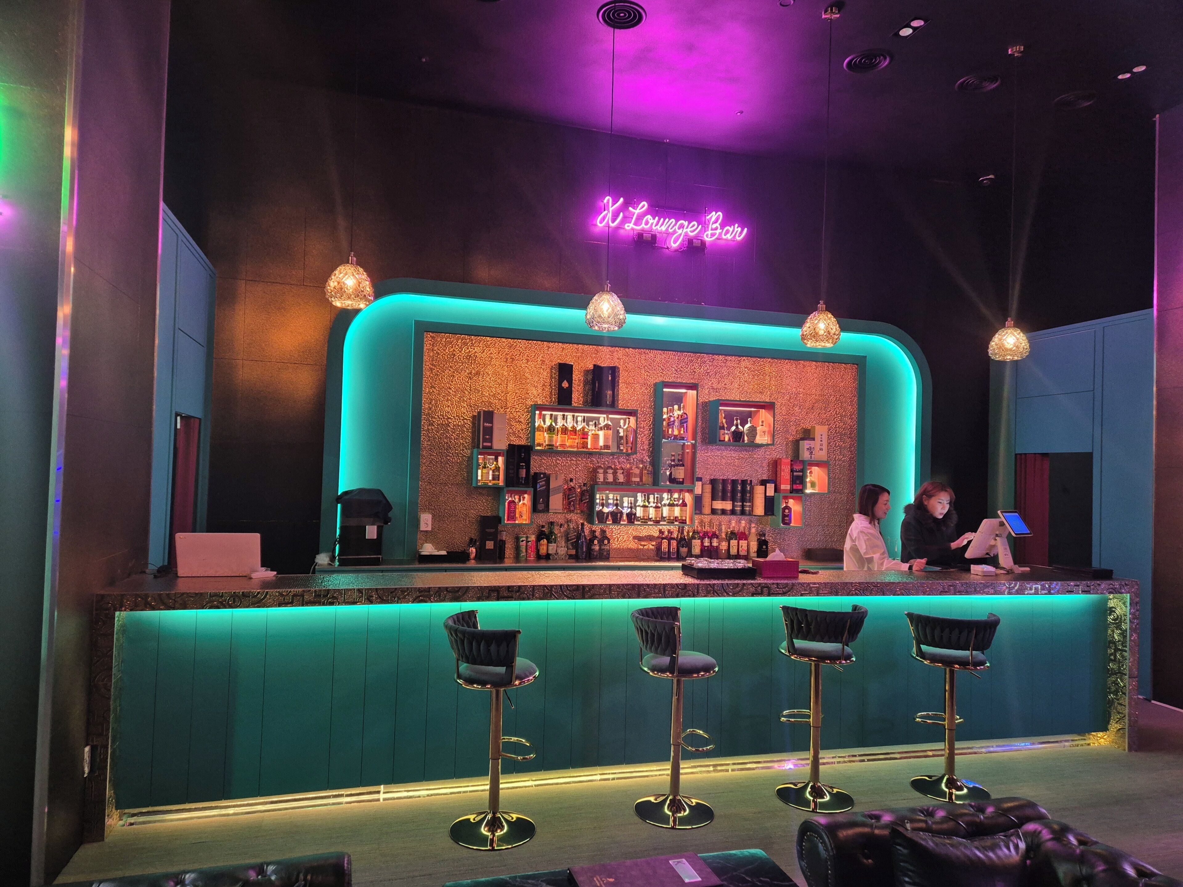Un espace bar avec un panneau néon, des tabourets de bar et un comptoir où sont exposées des bouteilles.