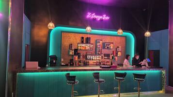 Zona de bar con letrero de neón, taburetes y mostrador con botellas.