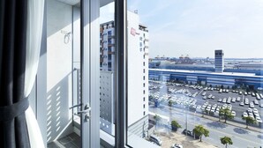 Vista da janela com grade de metal, com vista para um estacionamento e um edifício com a placa 'Coop Stay Hotel'.