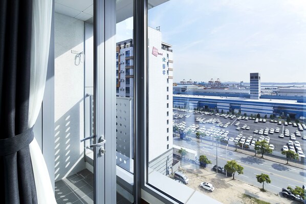 A view from a window with a metal railing, overlooking a parking lot and a building with a sign that reads 'Coop Stay Hotel'. - Ktree Pyeongtaek hotel (Pyeongtaek)