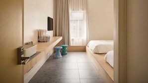 A modern hotel room with a wooden bench, a small round table, a bed, and a large window with curtains.