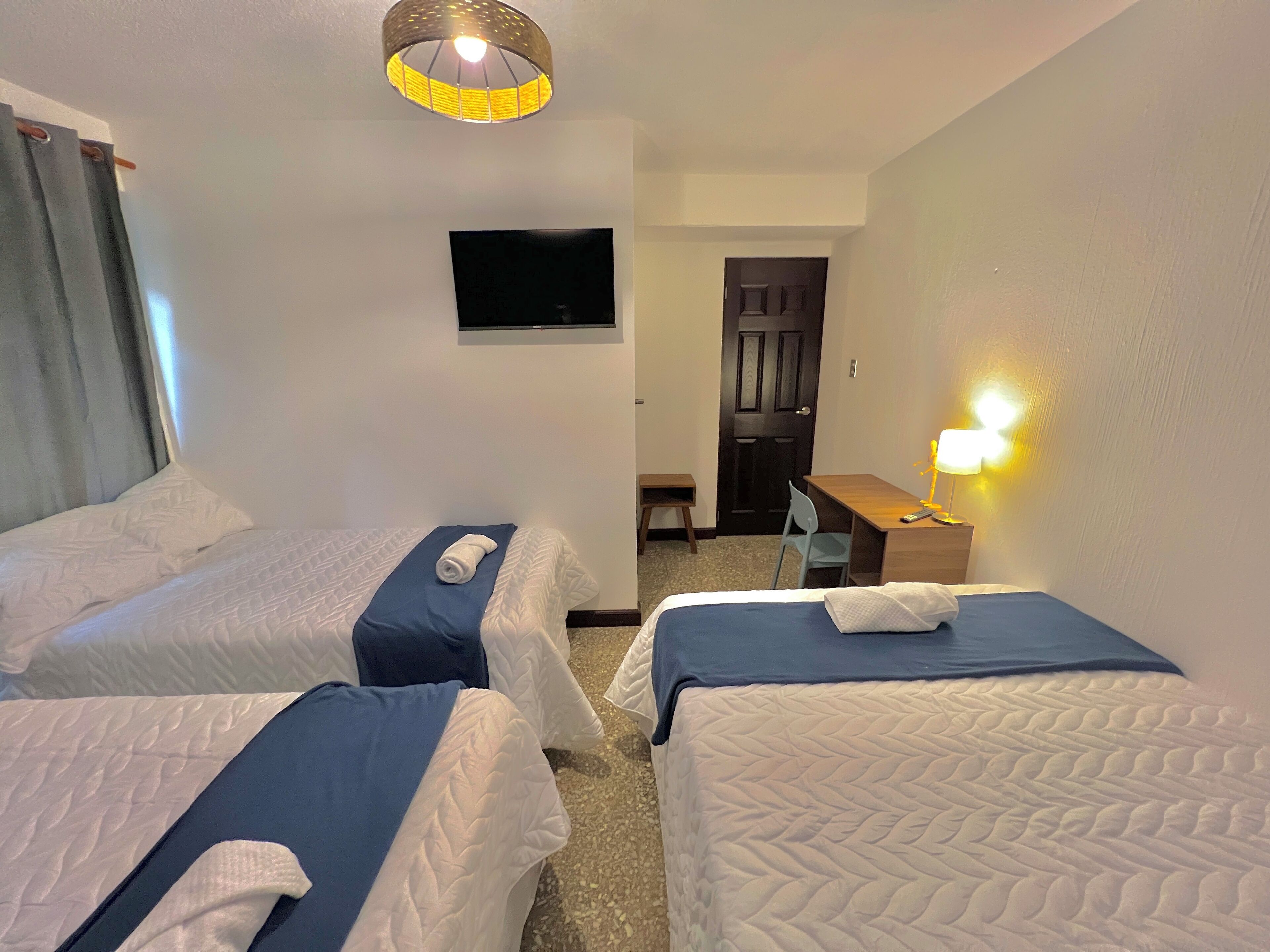 A hotel room with two beds, a desk, a chair, a television, and a lamp.