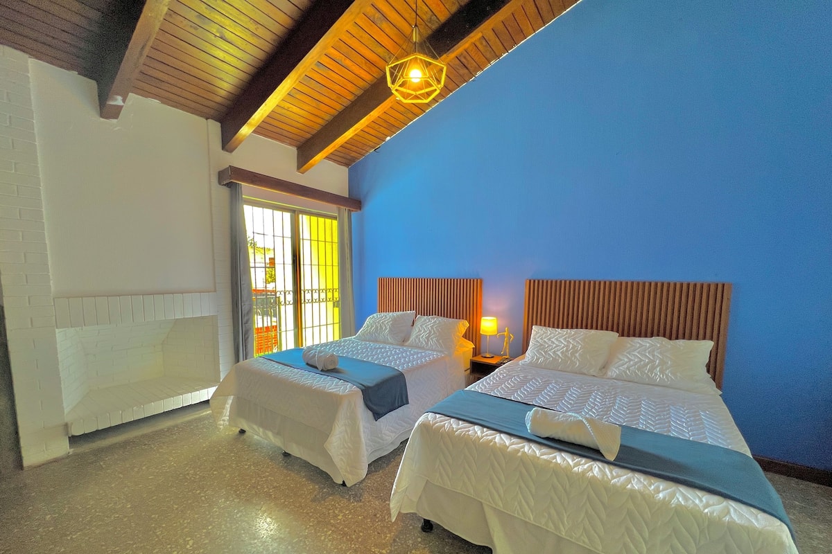 Une chambre d’hôtel avec deux lits, une cheminée en briques et un mur d’accent bleu.
