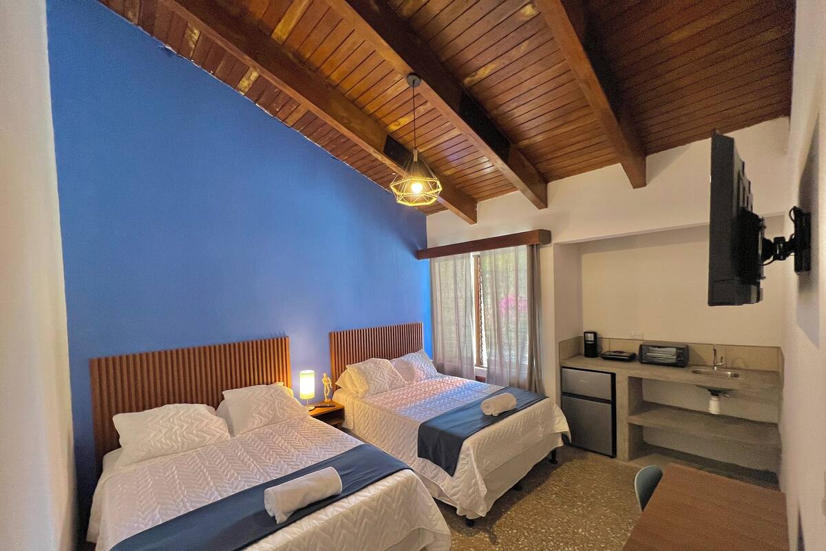 Une chambre d’hôtel avec deux lits, un bureau doté d’un lavabo et un téléviseur fixé au mur.