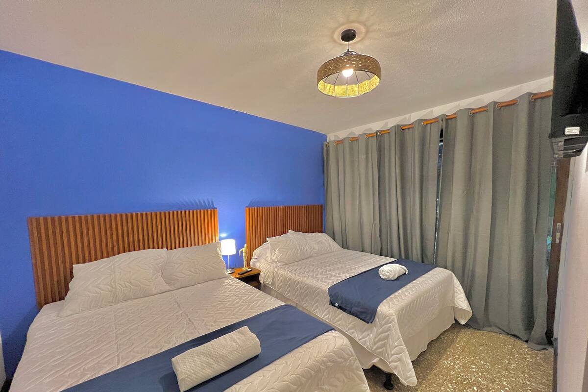 Une chambre d’hôtel avec deux lits, un luminaire au plafond et une fenêtre avec des rideaux.