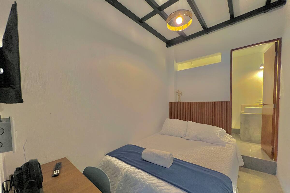 Une chambre d’hôtel équipée d’un lit, d’un bureau, d’une chaise, d’une télécommande et d’un téléviseur fixé au mur.