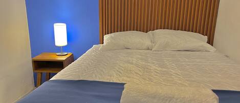 A neatly made bed with white linens, a blue blanket, and a folded white towel on the bed.