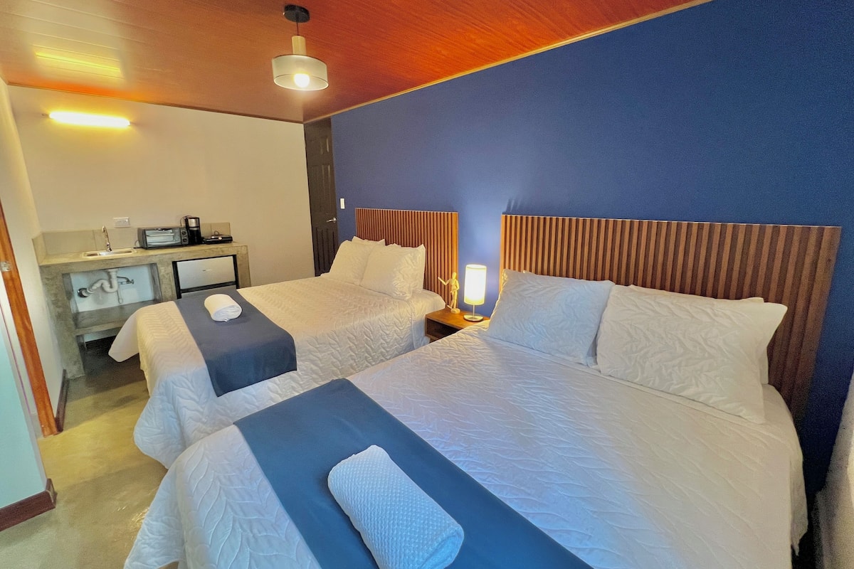 Une chambre d’hôtel avec deux lits, un bureau avec une machine à café et une table de chevet avec une lampe.