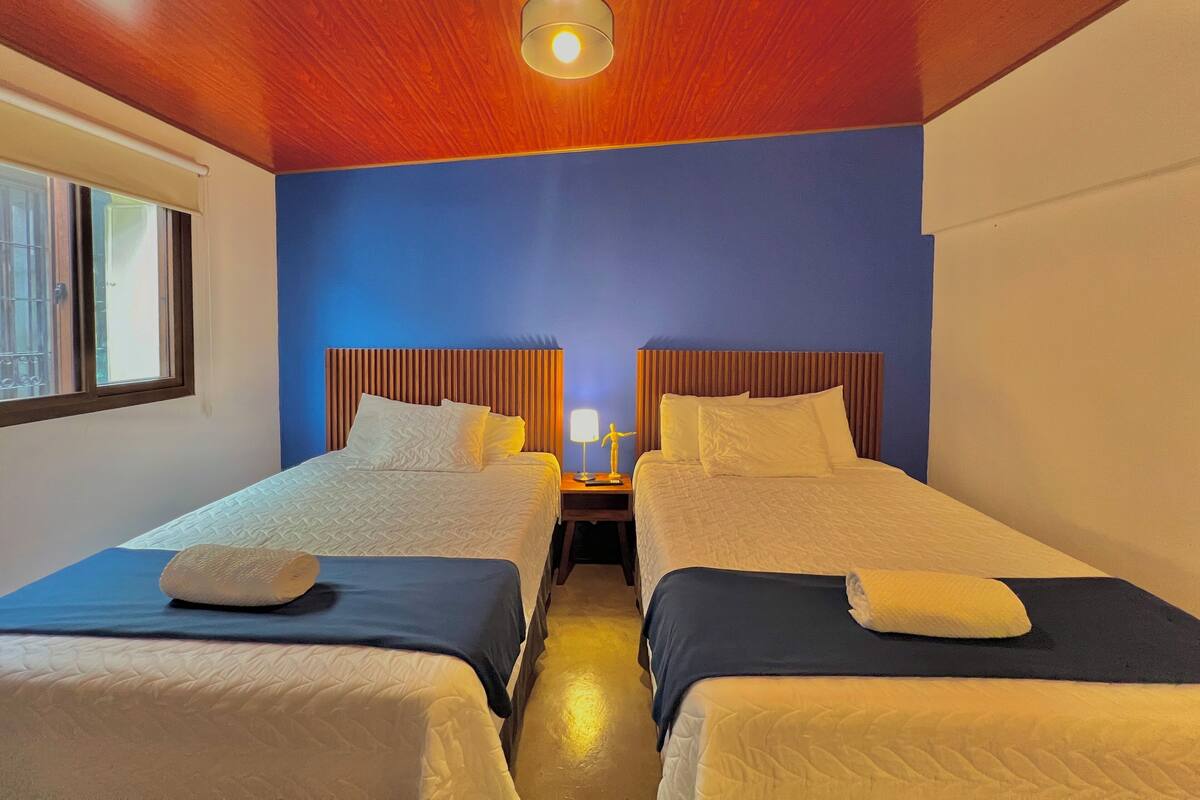 Une chambre d’hôtel avec deux lits, une table de chevet avec une lampe et une fenêtre avec des barreaux.