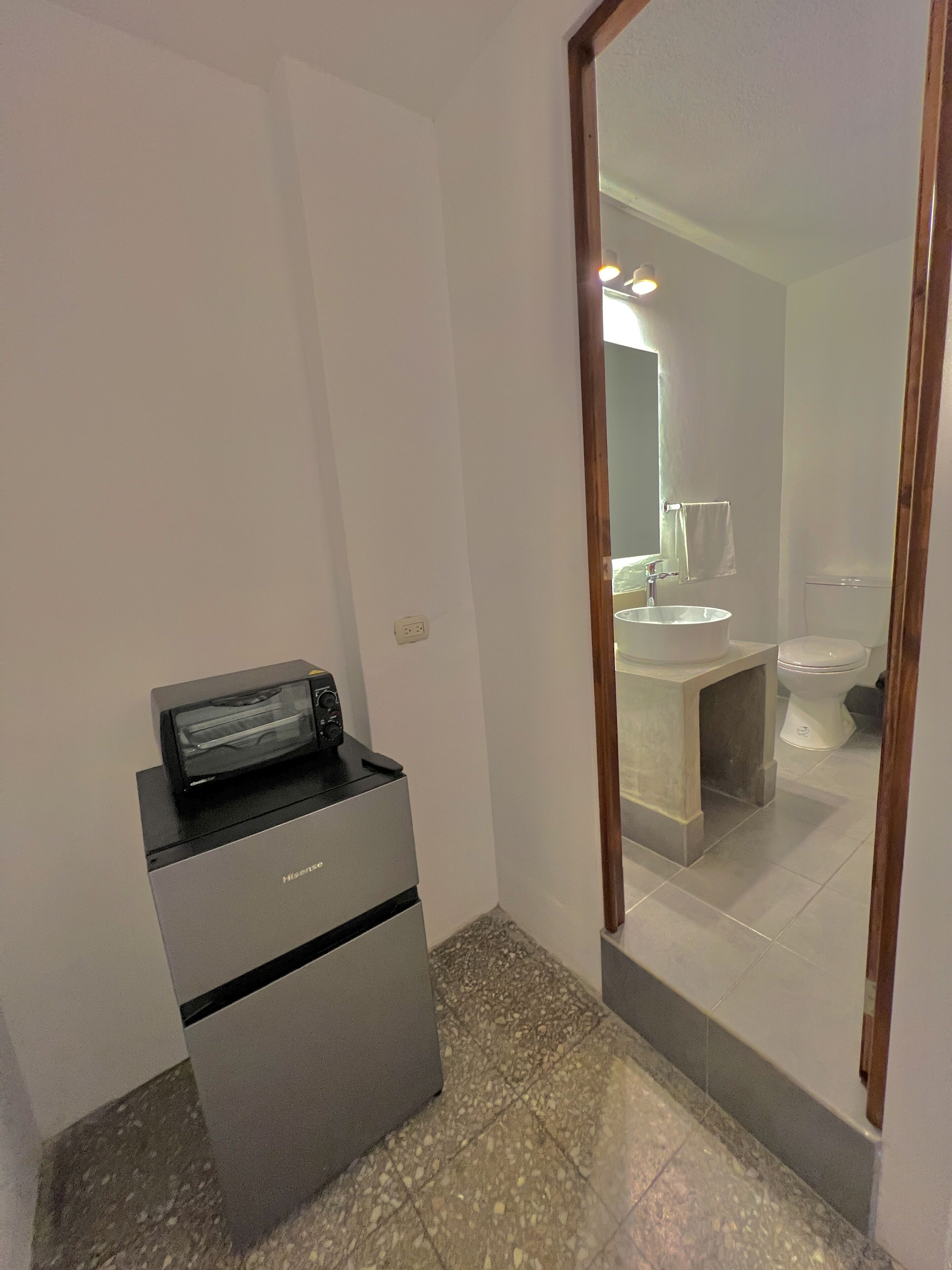 A compact hotel room with a small desk, a mirror, a sink, and a toilet.