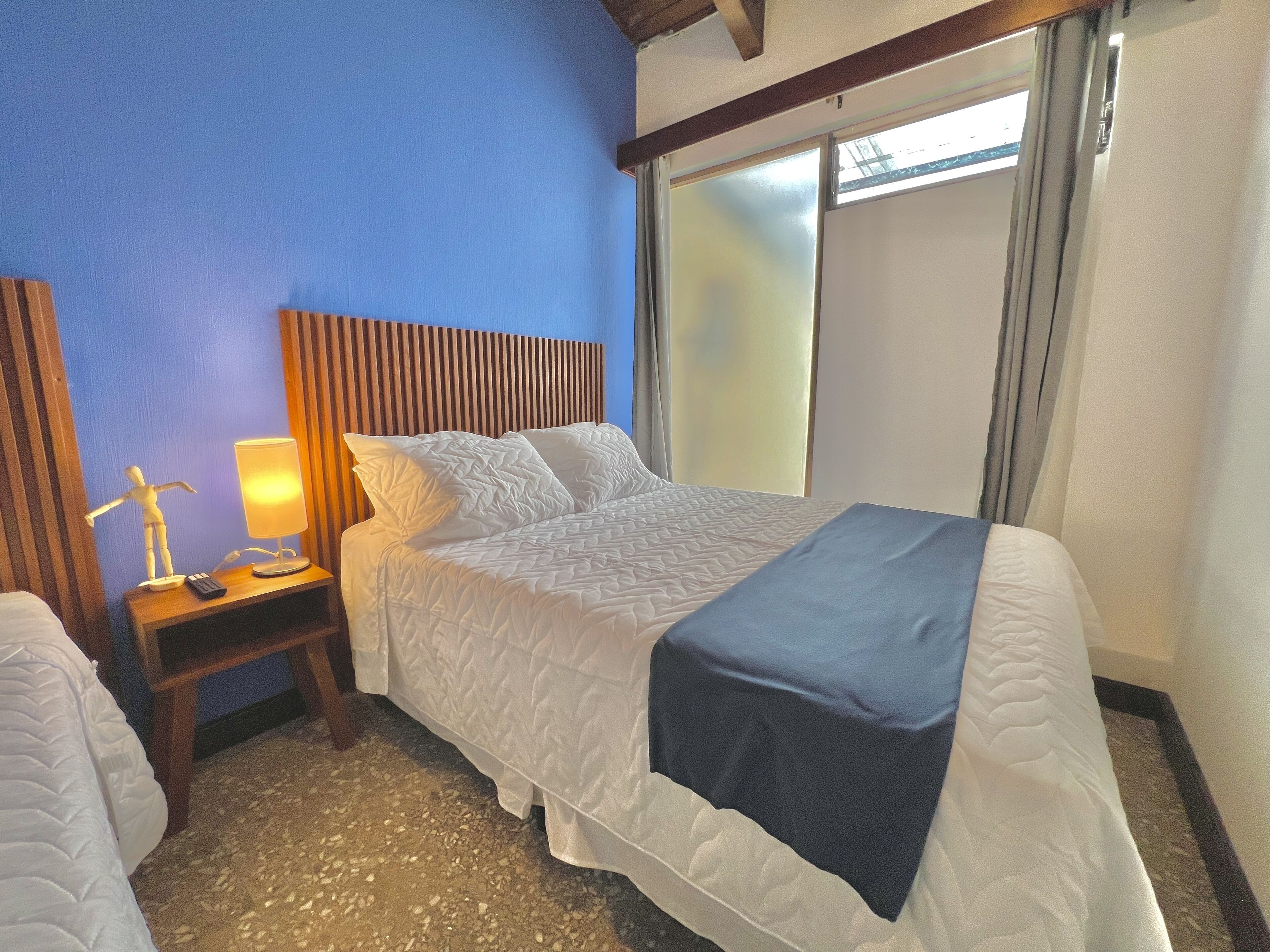 Ein Hotelzimmer mit Bett, Nachttisch, Lampe und einem Fenster mit Vorhängen.
